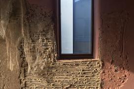 Photographie représentant la finition intérieure des murs en argile. La photographie permet de voir la natte en roseaux qui a été vissée dans le mur et sur laquelle l'argile est appliquée.